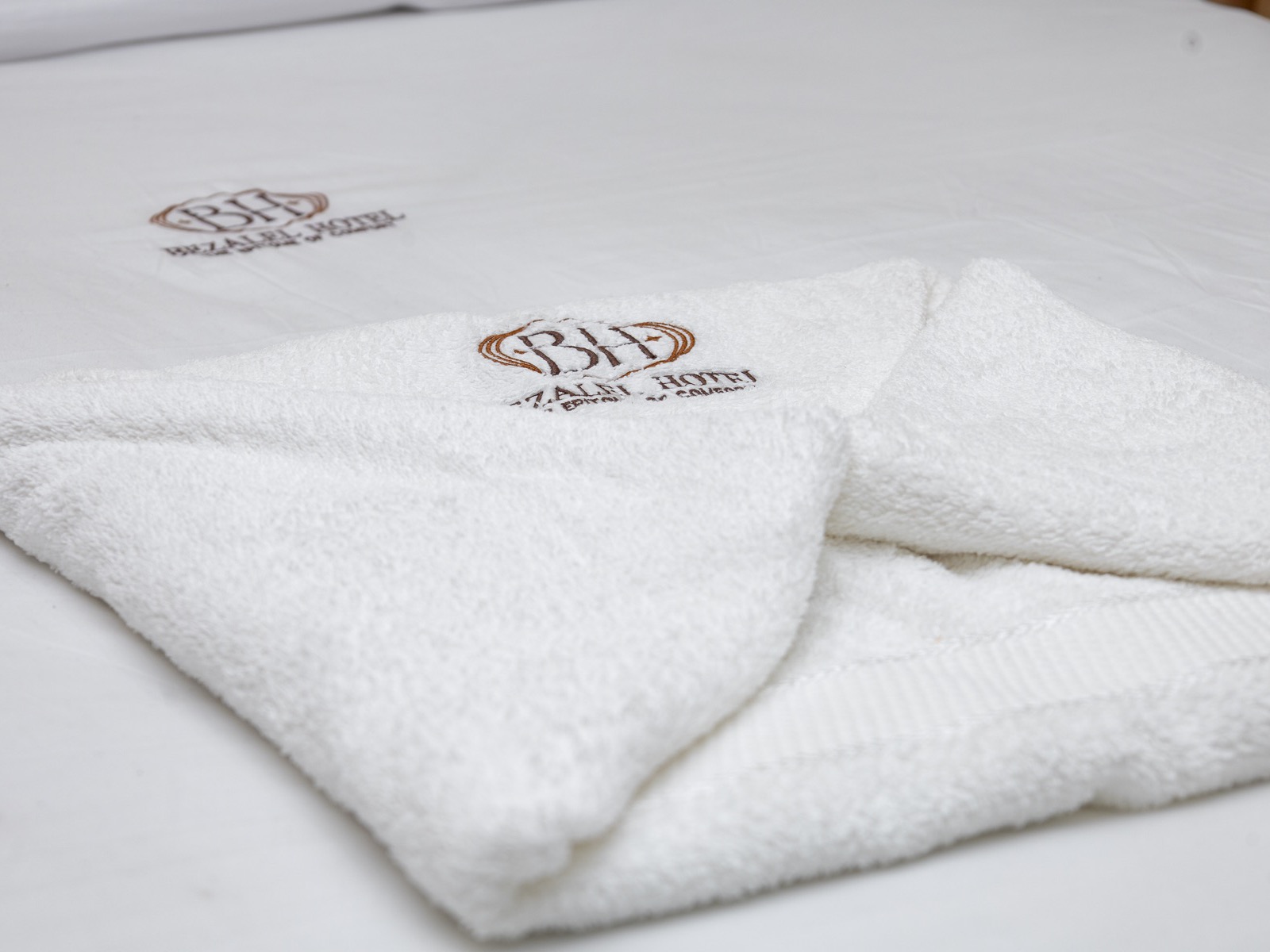 A folded towel with the BH monogram on the made-up bed